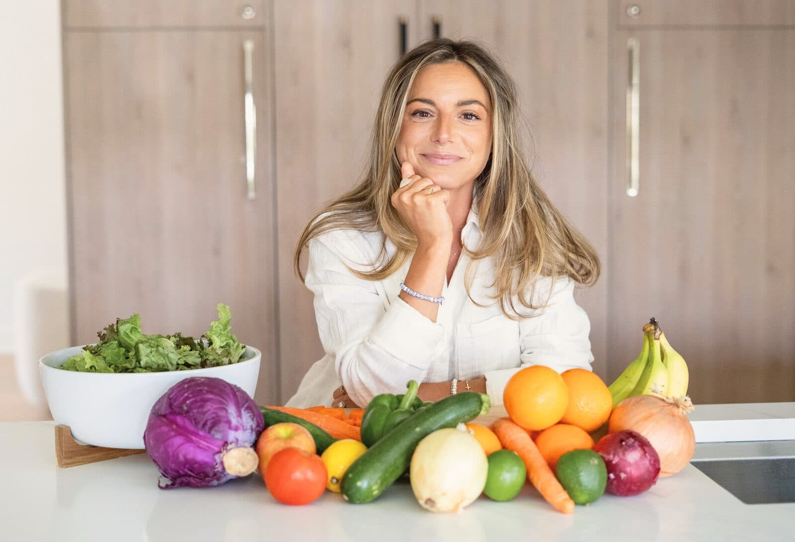 Danielle smiling with her chin on her hand behind a spread of fresh fruit and vegetables