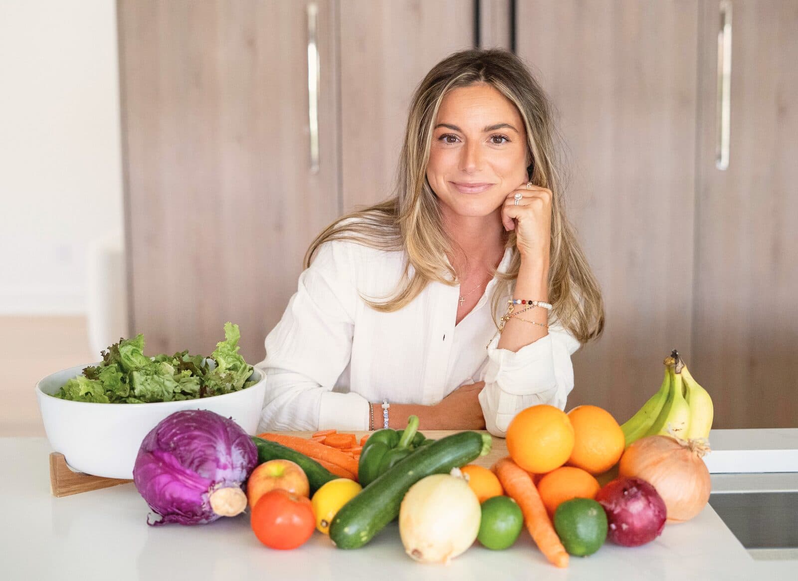 Danielle resting her chin in her hand behind a spread of fresh produce, smiling